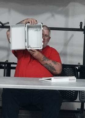 A person in a red shirt opening a box

Description automatically generated